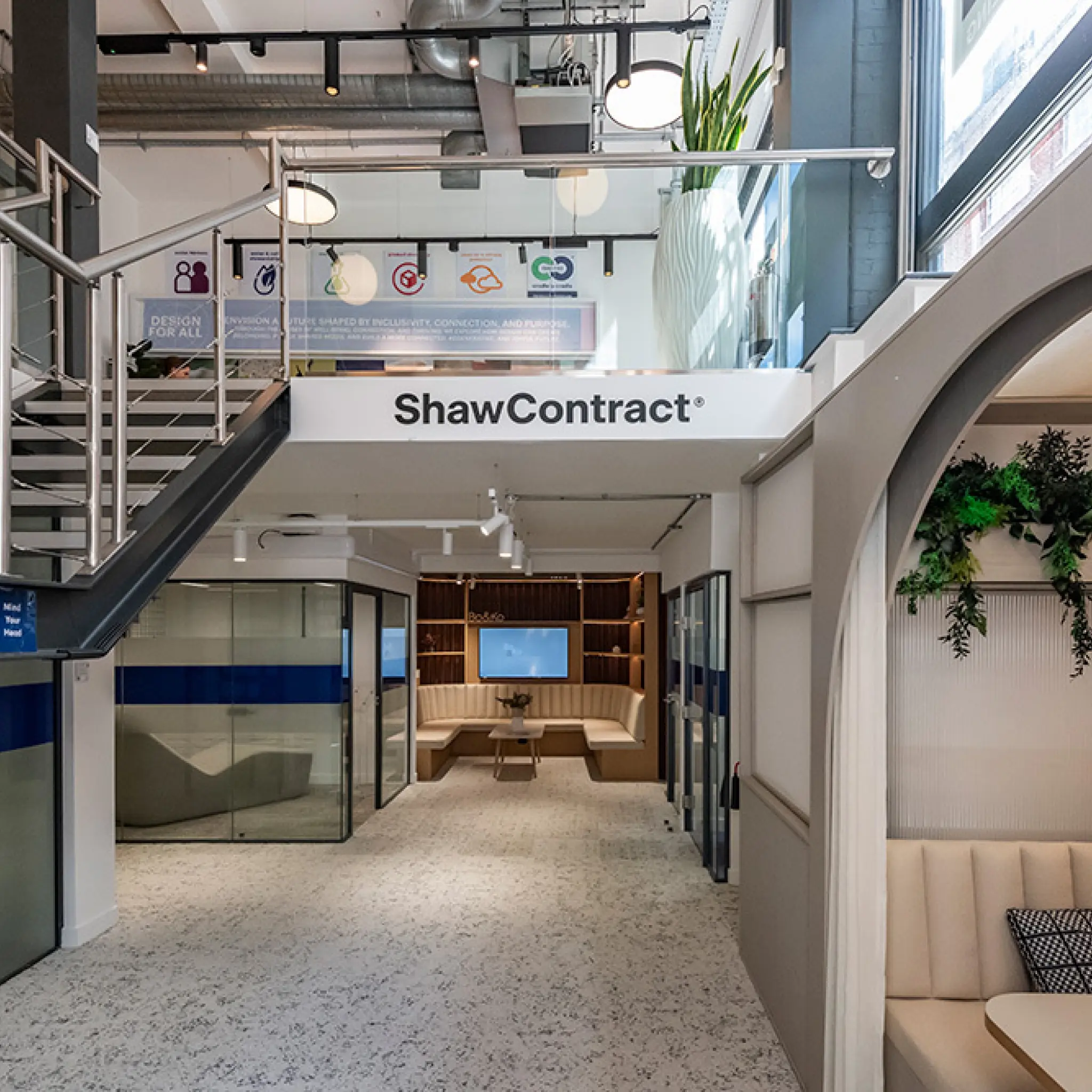 A modern office interior with a staircase, open workspace, seating areas, and prominent ShawContract branding.